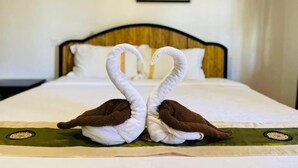 Un lit avec une tête de lit en bois, une couvre-lit verte et deux serviettes en forme de cygnes.