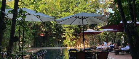 Uma área de piscina ao ar livre com espreguiçadeiras e guarda-sóis, rodeada por vegetação exuberante.