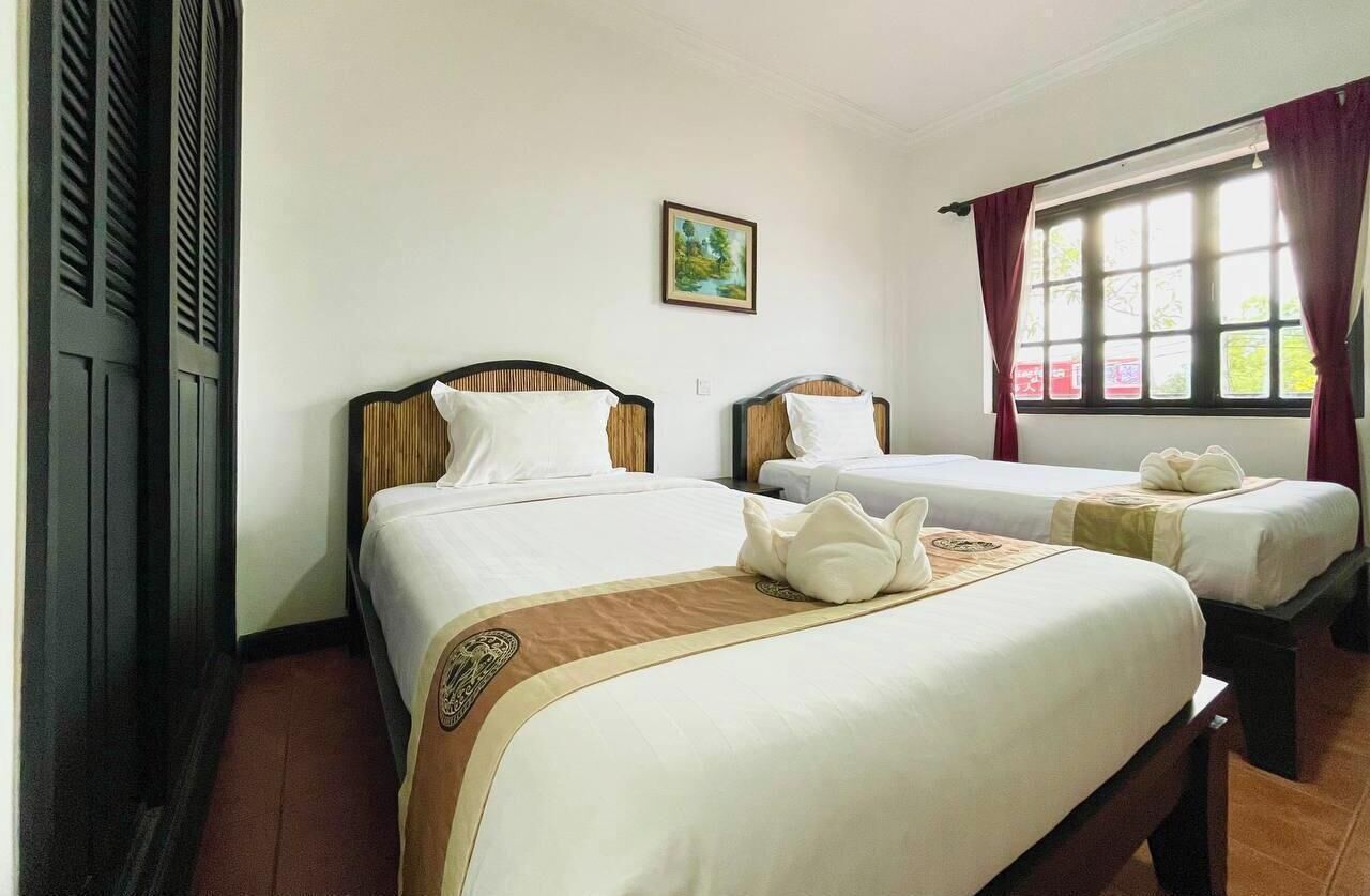 A hotel room with two beds, a window with curtains, and a painting on the wall.