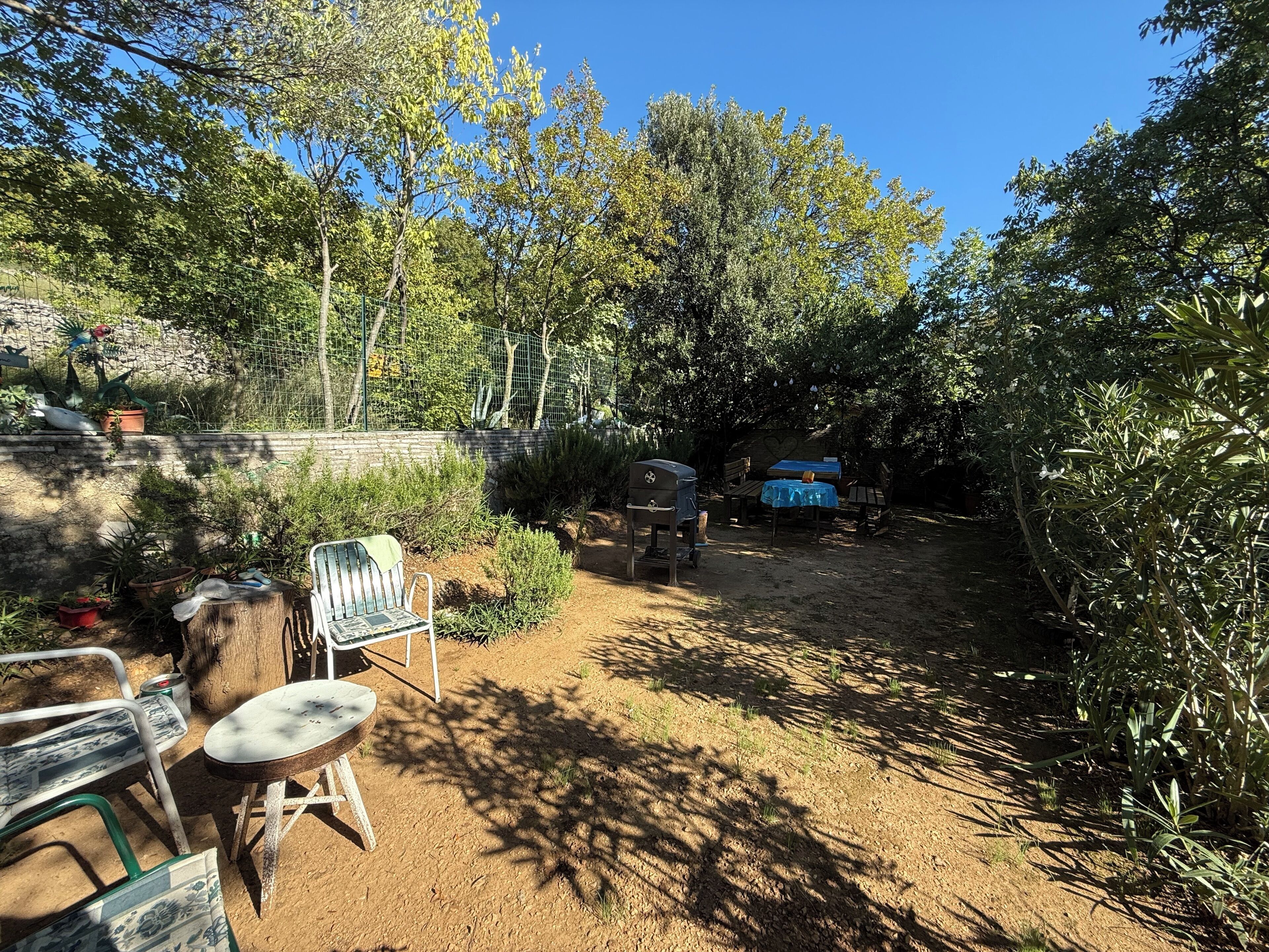 Un espace extérieur aménagé en terrasse, avec un barbecue, une table recouverte d’une nappe bleue et plusieurs chaises.