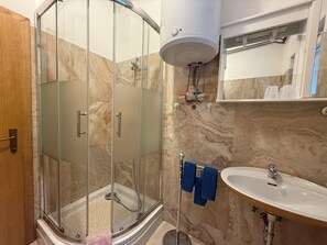 Ein Badezimmer mit einer Glaskabine zur Dusche, einem weißen Waschbecken und einer Wand mit Marmorplatten.