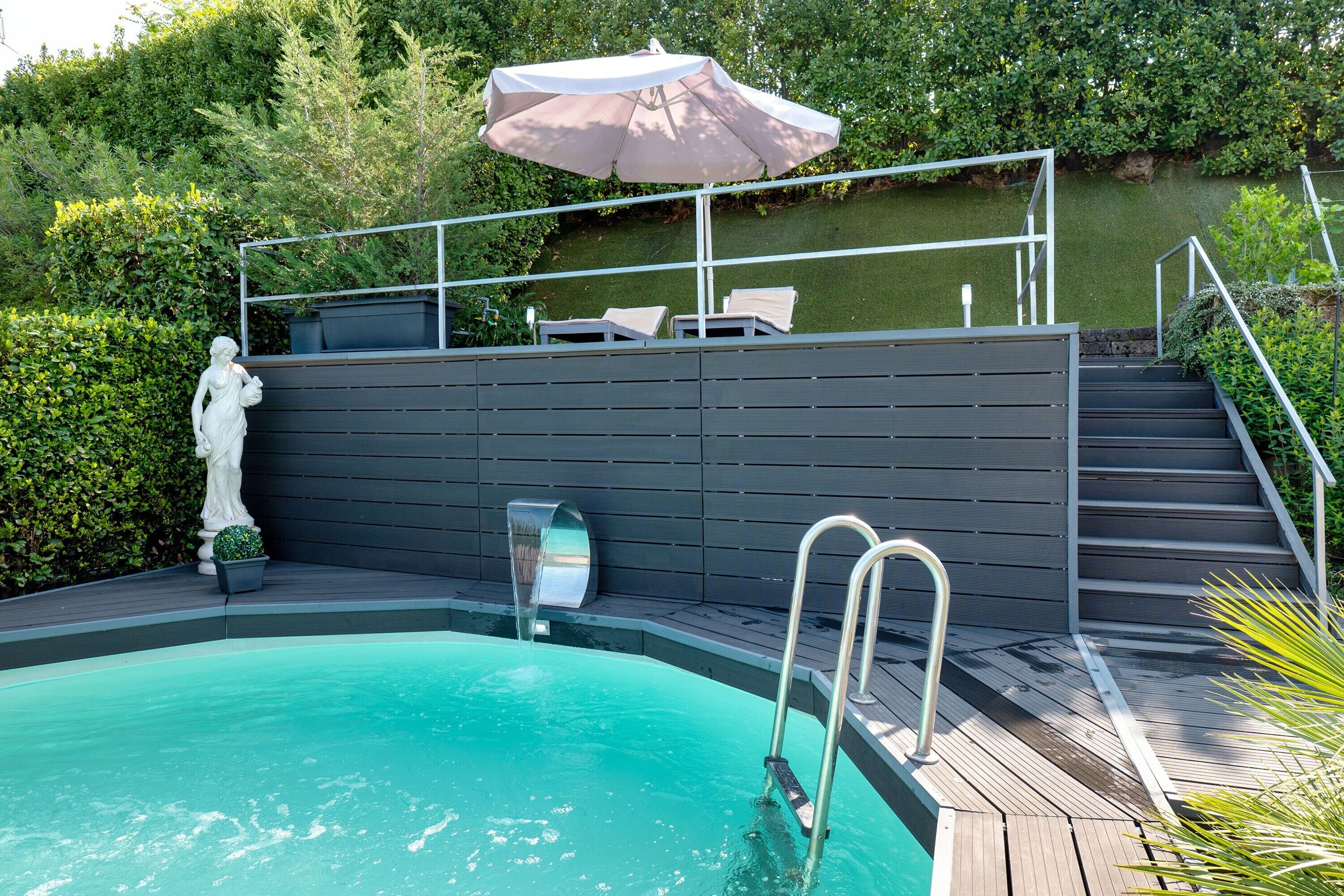A swimming pool with a metal ladder, a statue, and a covered seating area with an umbrella.