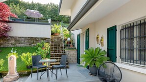 Eine Terrasse mit Tisch und Stühlen, einem Blumentopf, einer Steinmauer und einer Treppe zu einem Balkon.