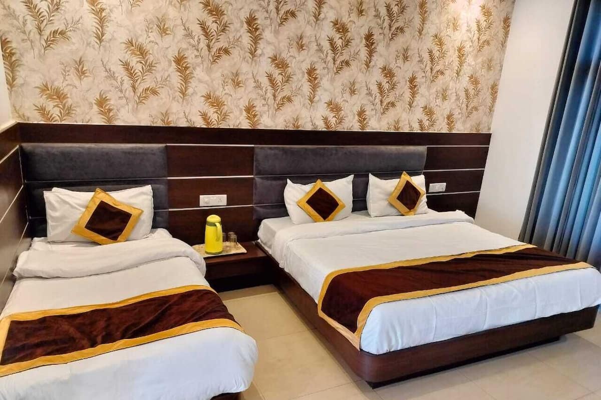 A hotel room with two beds, dark wood headboards, white bedding with brown accents, a patterned wallpaper, and a blue curtain.
