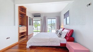 Un dormitorio con una cama grande, un armario de madera, una mesita de noche rosa y vistas al exterior a través de una puerta corrediza de vidrio.