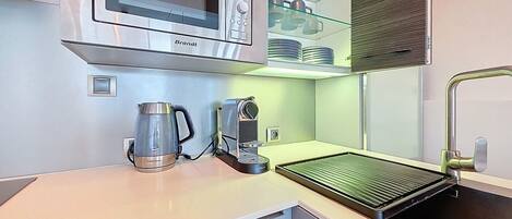 Una cocina moderna con un microondas de acero inoxidable, una cafetera y un hervidor sobre la encimera.