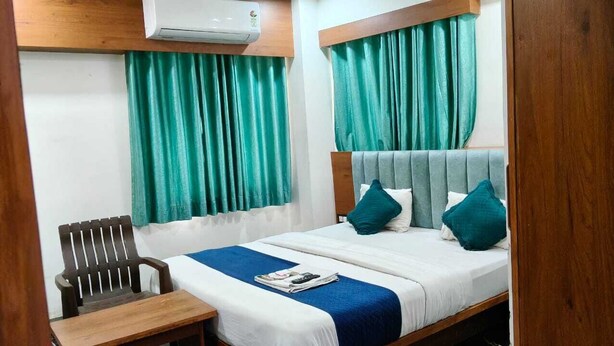 Une chambre d’hôtel avec un lit double, une table de chevet en bois, une chaise et des rideaux verts.
