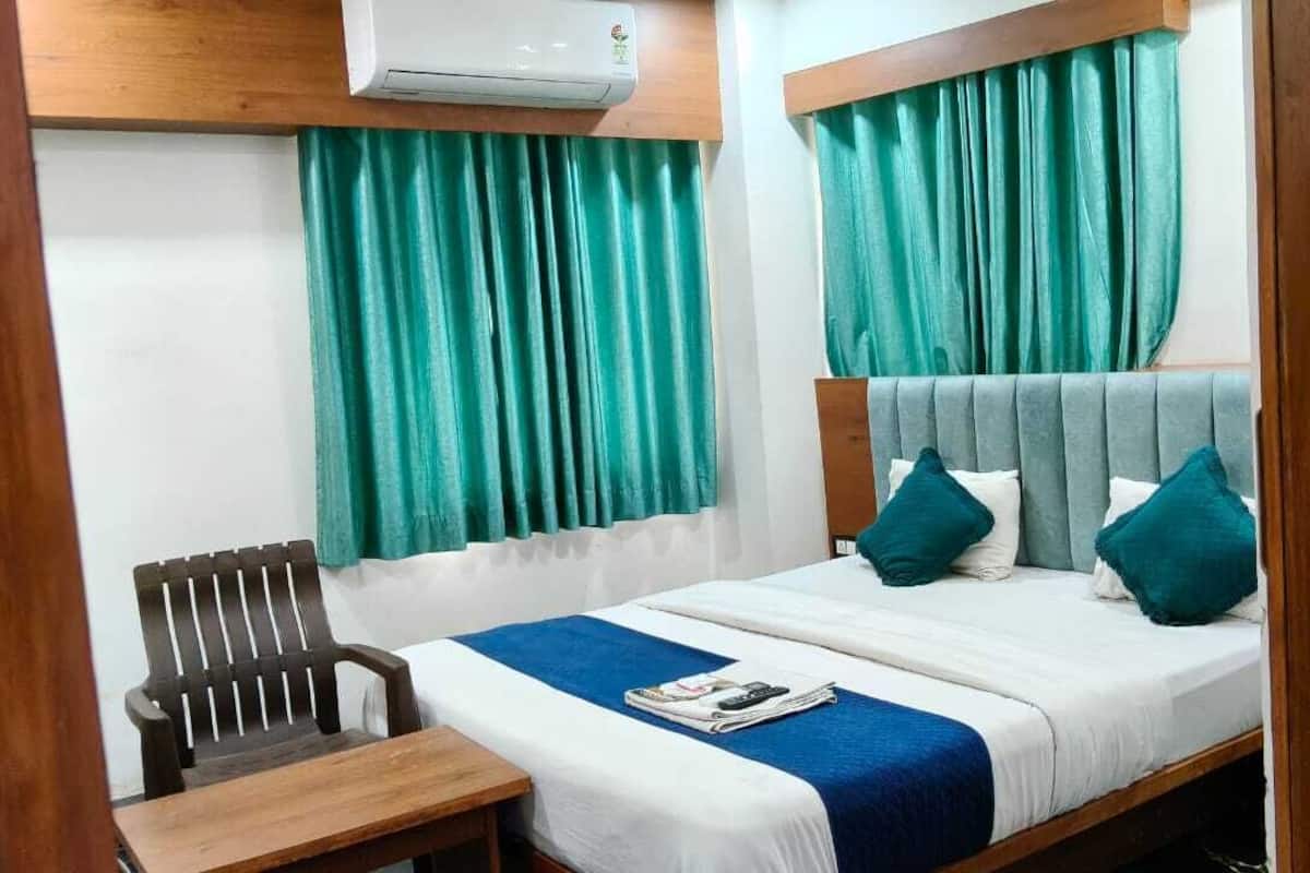 Une chambre d’hôtel avec un lit, une chaise en bois, une table et une fenêtre avec des rideaux.
