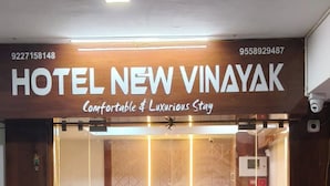 L’entrée de l’hôtel New Vinayak se distingue par un tapis rouge, un comptoir d’accueil en bois et un intérieur moderne visible à travers les portes vitrées.