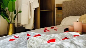 Hotellihuone, jossa on sänky, vaatekaappi, seinälle ripustettu kylpytakki, ruukussa oleva kasvi ja seinään asennettu ilmastointilaite.