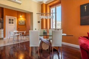 A dining area with a glass table and chairs, a chandelier, and a city view through a window. - Cosy and comfortable flat located in the heart of Cagliari. (Cagliari)