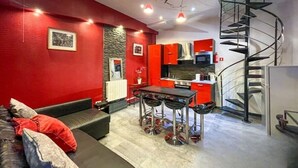 Een moderne keuken met rode kasten, een zwarte spiraaltrap en een eetgedeelte met een zwarte tafel en krukken.