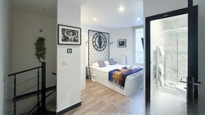 Een moderne slaapkamer met een bed, een klok aan de muur, en een zichtbare badkamer door een open deur.