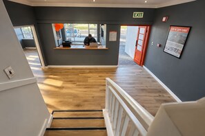 A hotel lobby with a wooden floor, a reception desk, and an exit sign.