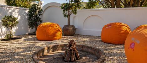 A courtyard with a central fire pit, surrounded by orange bean bags and potted plants.