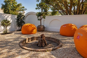 A courtyard with a central fire pit, surrounded by orange bean bags and potted plants. - never@home Hermanus (Hermanus)