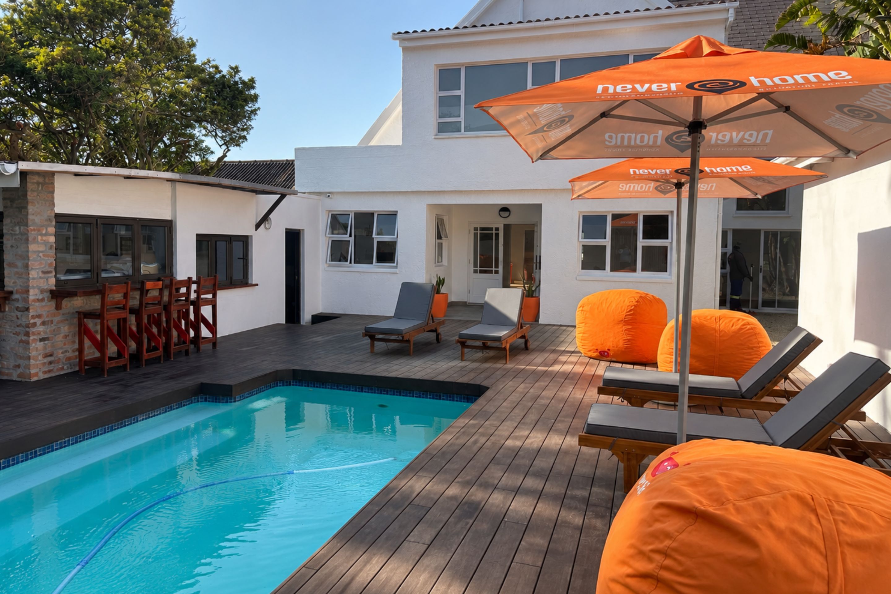 Un espace piscine avec des chaises longues et un parasol, entouré d’une terrasse en bois et d’un bâtiment blanc.