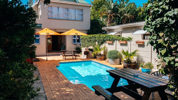 A backyard with a swimming pool, a picnic table, and two yellow umbrellas. - never@home Hermanus (Hermanus)