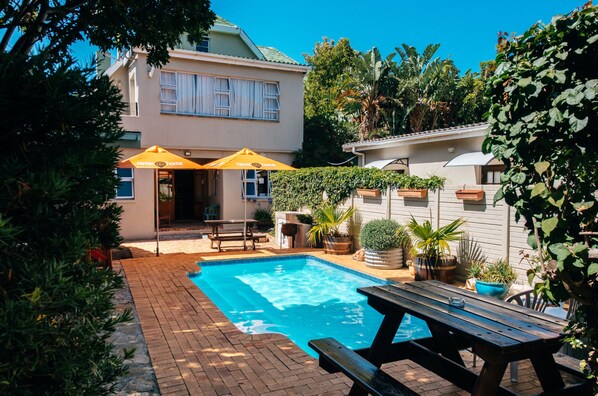 A backyard with a swimming pool, a picnic table, and two yellow umbrellas. - never@home Hermanus (Hermanus)