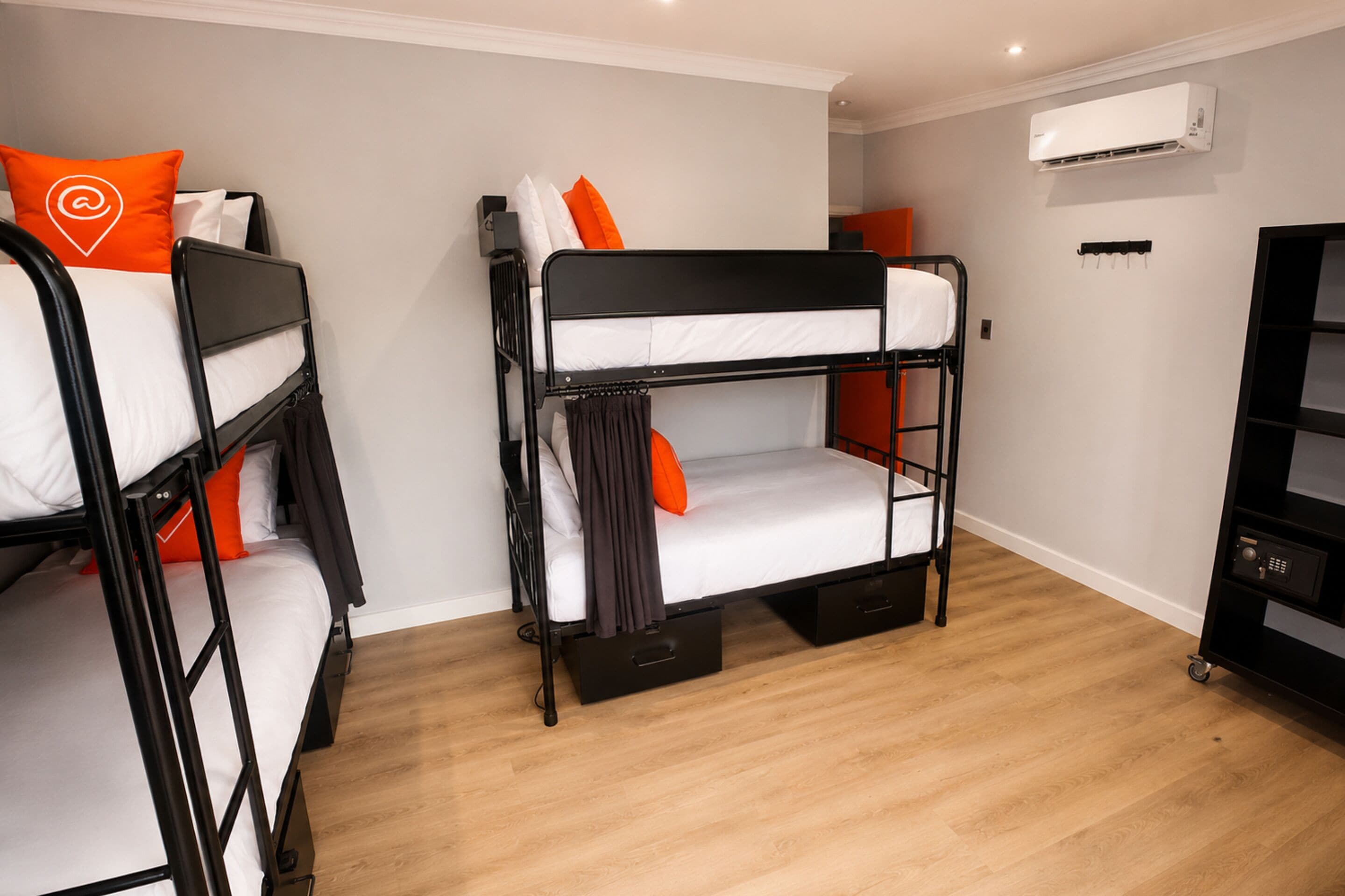 A bunk bed room with a wooden floor, an air conditioning unit on the wall, and a black storage unit with a lock.