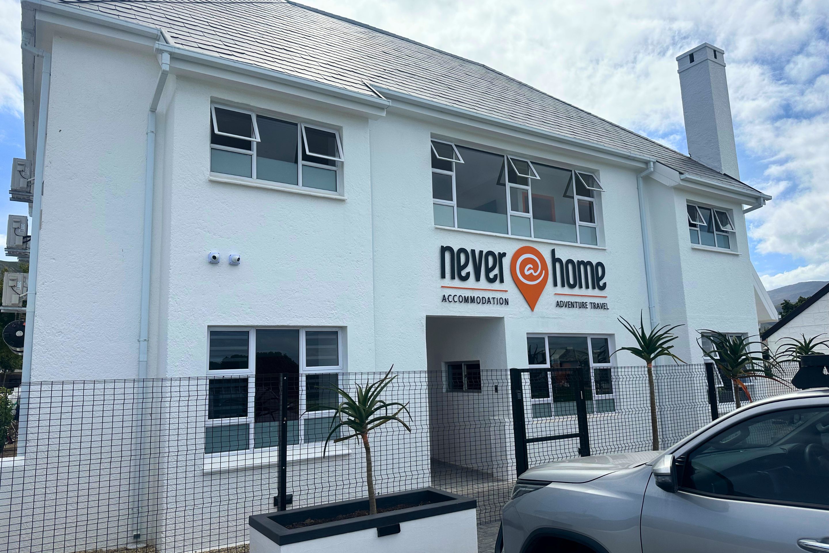 Un edificio bianco con un cartello che recita 'Never Home Accommodation Adventure Travel'.