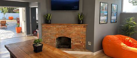 A modern living room with a brick fireplace, a wooden dining table, and a large orange bean bag.