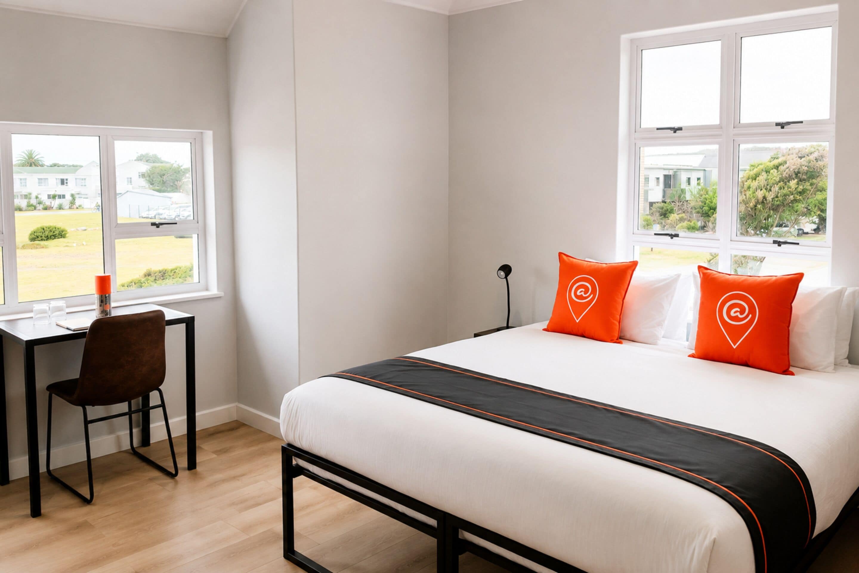 Una habitación de hotel con una cama, un escritorio y dos ventanas.