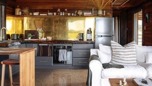 A rustic cabin interior with a wooden ceiling, a kitchen with modern appliances, a white sofa, and a dining area.