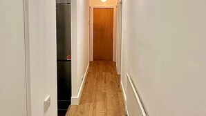 A narrow hallway with wooden flooring, white walls, and a ceiling light fixture. - Finchley Ground Floor Apartment (London)