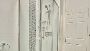 A glass-enclosed shower with a tiled wall and a white door in the background. - Finchley Ground Floor Apartment (London)