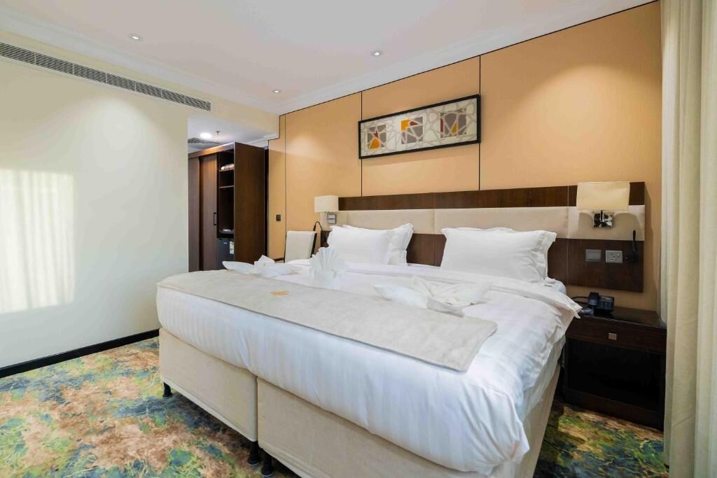 Une chambre d’hôtel avec un grand lit, des tables de chevet, une tête de lit, une œuvre d’art accrochée au mur et une armoire.