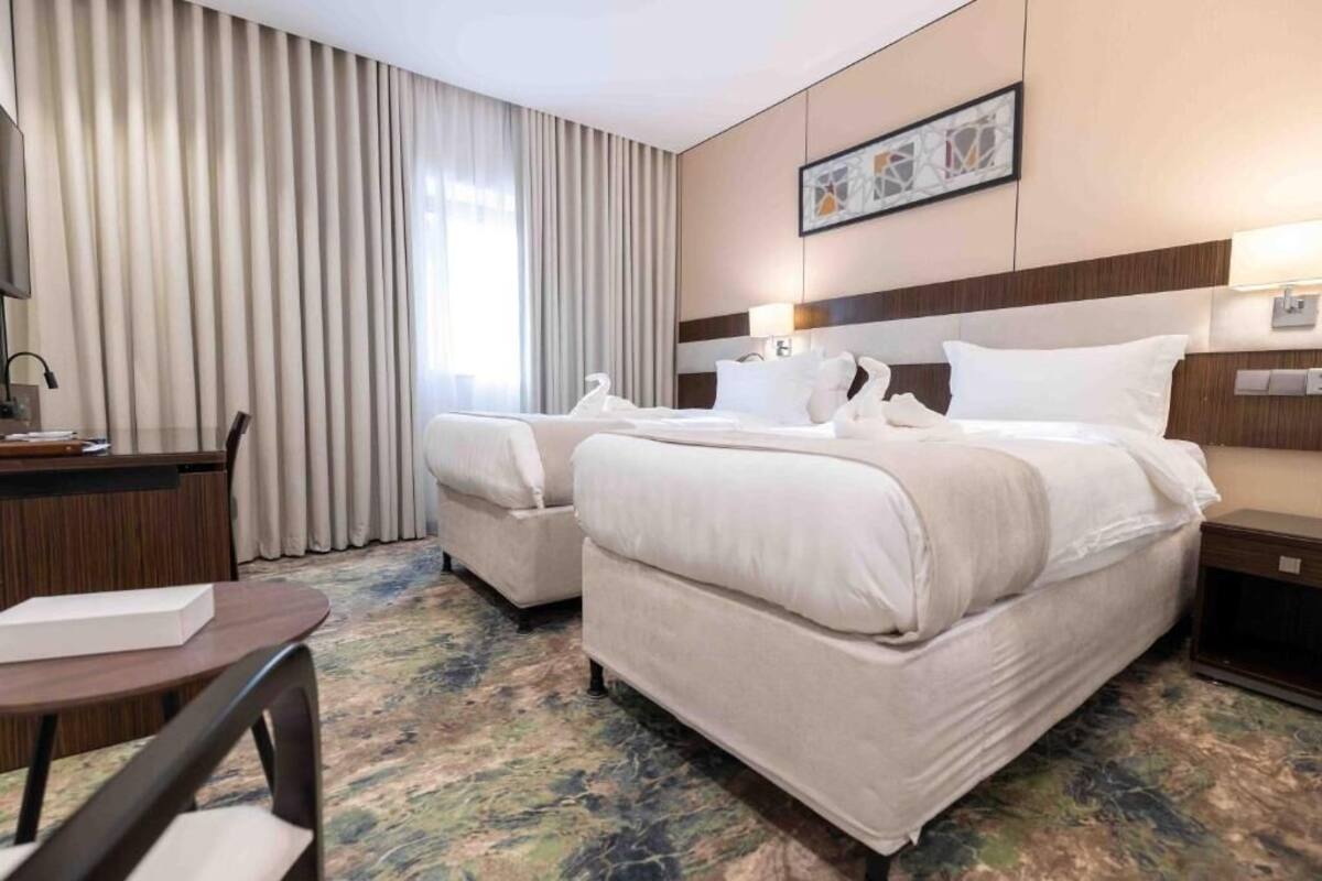 Quarto de hotel com duas camas, uma escrivaninha e uma cadeira.