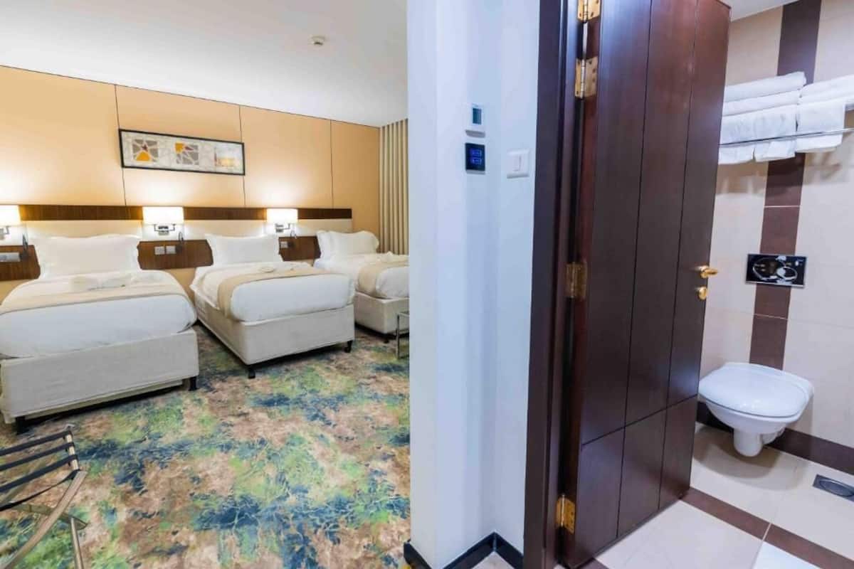 Quarto de hotel com duas camas, banheiro com vaso sanitário e chuveiro.