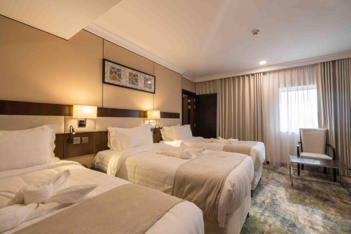 Quarto de hotel com três camas, uma escrivaninha e uma cadeira.