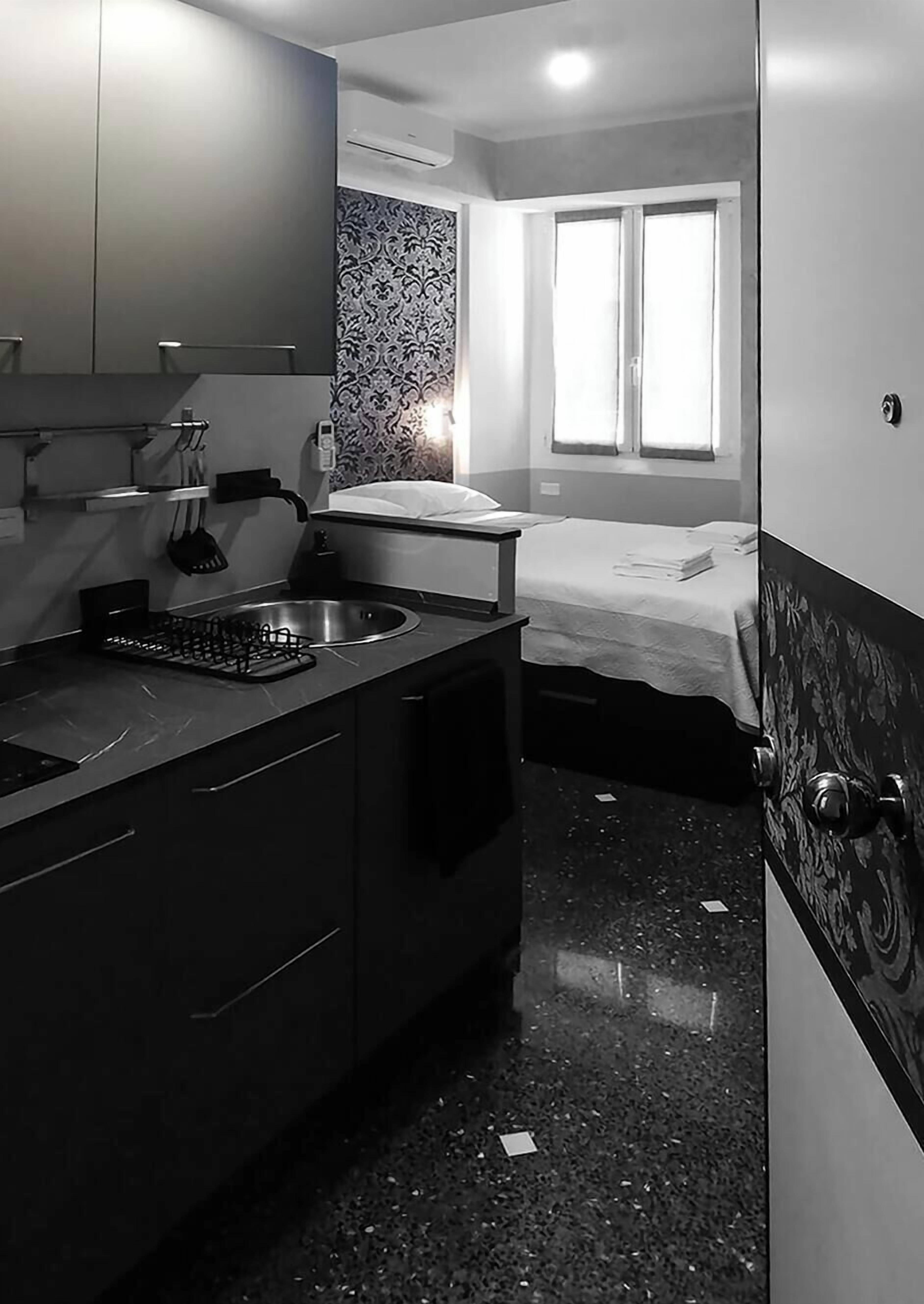 Una habitación de hotel compacta con kitchenette, una cama, un ventanal y un papel tapiz estampado.