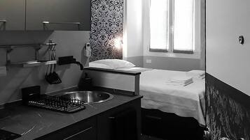 Una habitación de hotel compacta con kitchenette, una cama, un ventanal y un papel tapiz estampado.