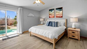 A bedroom with a bed, bedside lamps, a ceiling fan, and a view of a swimming pool. - Breakwater Retreat | Pool, Spa, Game Room, Boat Parking (Lake Havasu City)