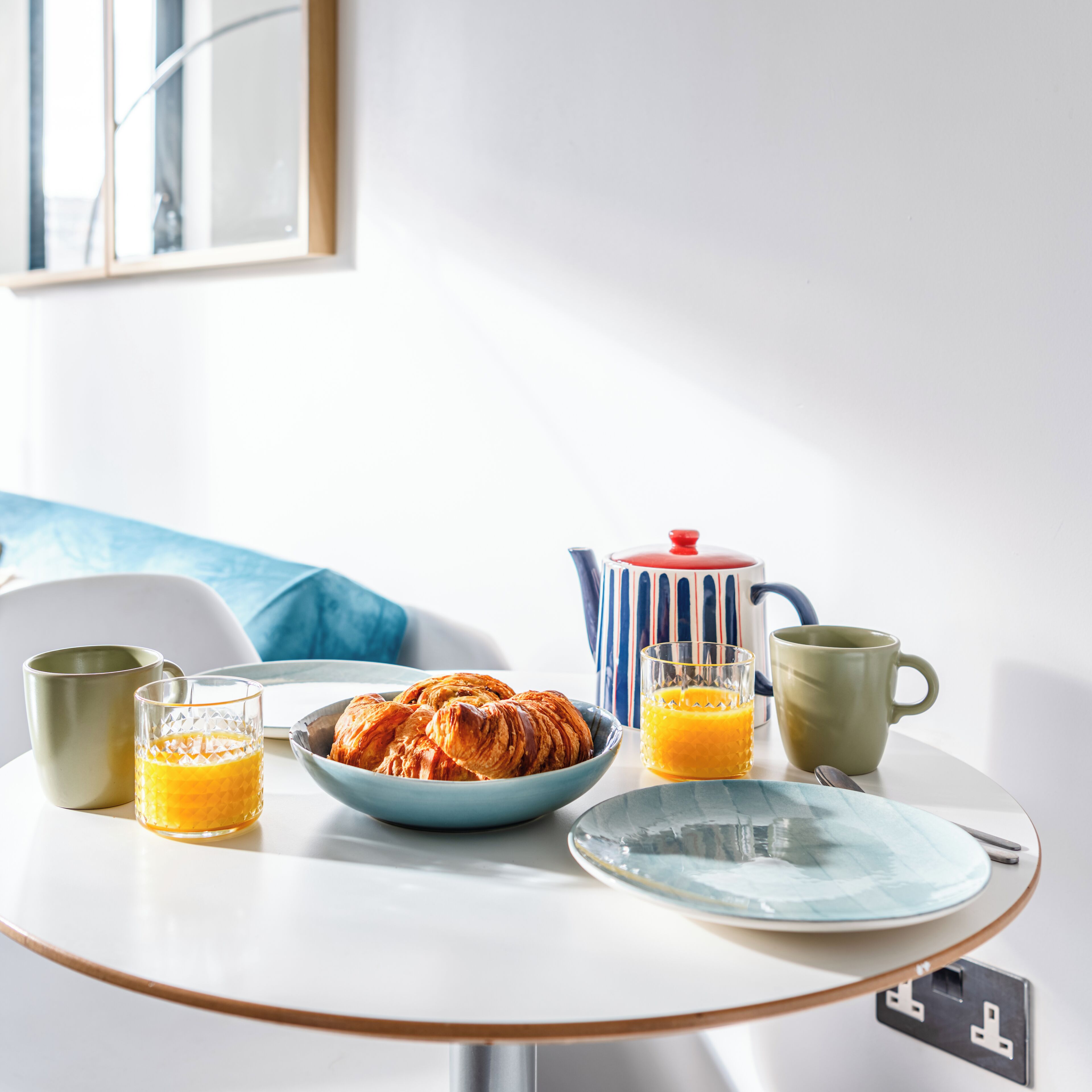 A breakfast table with croissants, orange juice, and a teapot.
