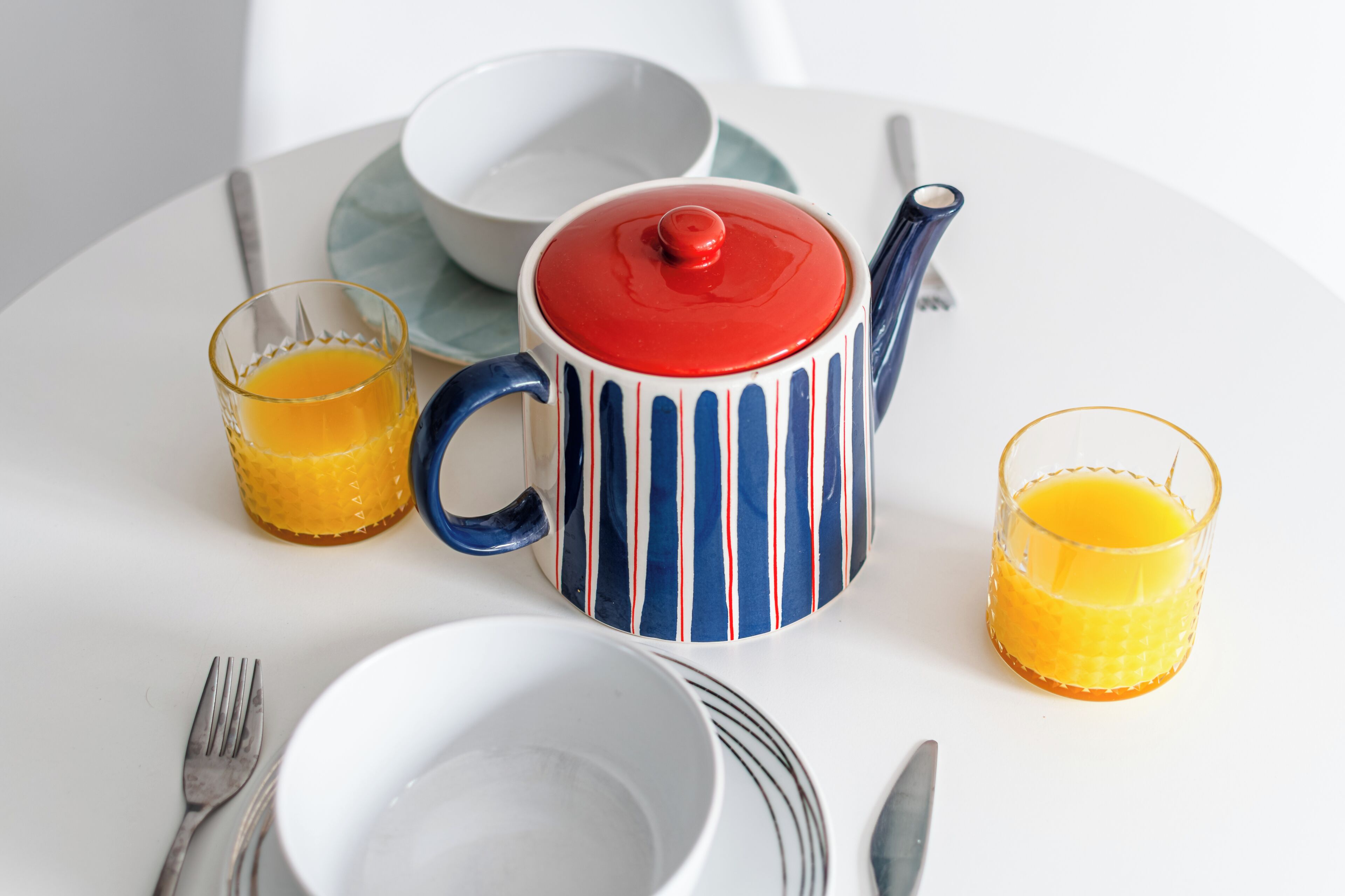 A table with a teapot, two glasses of orange juice, a bowl, and cutlery.