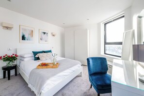 Ein modernes Schlafzimmer mit einem Bett, einem Nachttisch mit Blumen, einem Stuhl, einem Schreibtisch und einem großen Fenster.