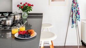 Een moderne keuken met een fornuis, een eethoek met krukken, en een schilderij aan de muur.