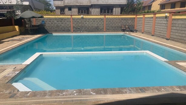En rektangulär swimmingpool med ett kaklat poolområde, omgiven av en låg stenmur och ett metallstaket som är försett med taggtråd.