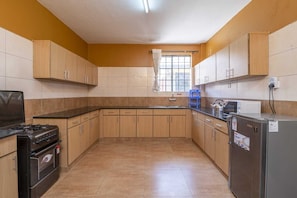 A kitchen with wooden cabinets, a stove, a refrigerator, and a window with curtains. - Gorgeous 3-bedroom bungalow in tranquil Kitengela perfect for relaxing. (Kitengela)