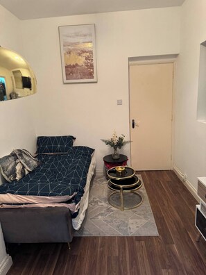 A bedroom with a bed, a small round table with a vase, a door, and a painting on the wall. - Modern 1-bedroom Flat in Trendy Leytonstone (London)