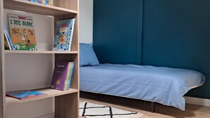 Un dormitorio con cama, una estantería llena de libros, una lámpara colgante y suelo de madera.