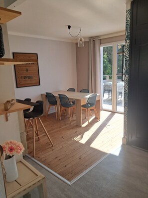 A modern dining area with a wooden table and chairs, a hanging light fixture, and a view of the outdoors through a glass door. - Villa Coat Ar Mor, 700m from the beach (TREVOU-TREGUIGNEC)