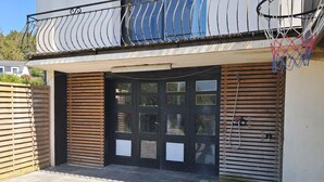 Una entrada de edificio con una puerta negra, una cerca de madera y un aro de baloncesto.
