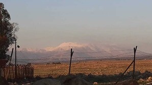 A fenced field with a mountain in the background. - Nomad truck in the Golan hights (Bruchim Qela' Alon)