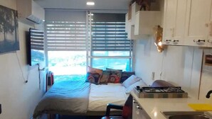 A compact bedroom with a bed, a small stool, and a window with blinds. - Nomad truck in the Golan hights (Bruchim Qela' Alon)