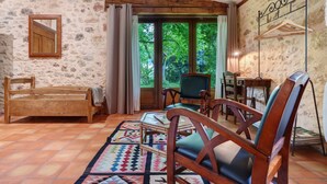A rustic room with a stone wall, wooden furniture, a large window, and a view of greenery. - Charming Cottage in Biron (Biron)
